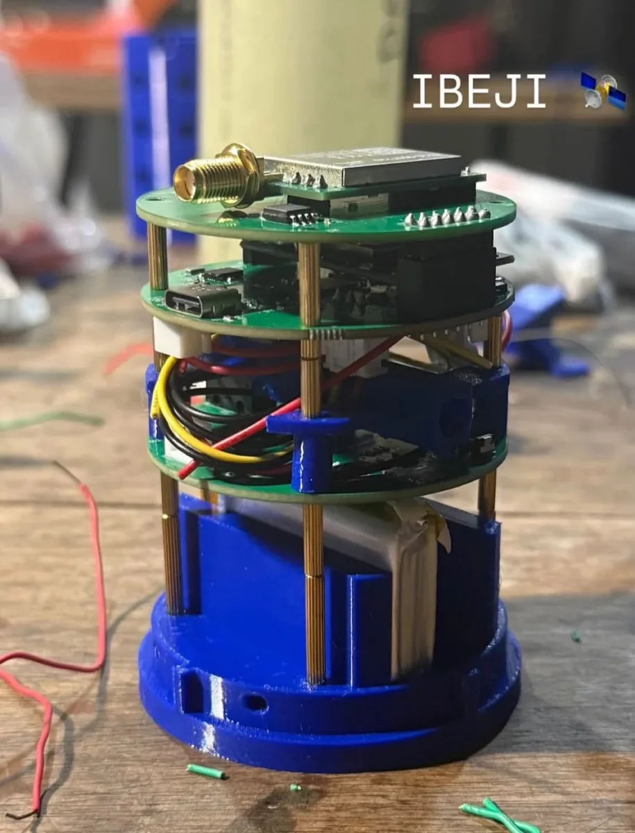Satélite IBEJI montado: placas de circuito empilhadas sobre uma base azul impressa em 3D, com antena e bateria